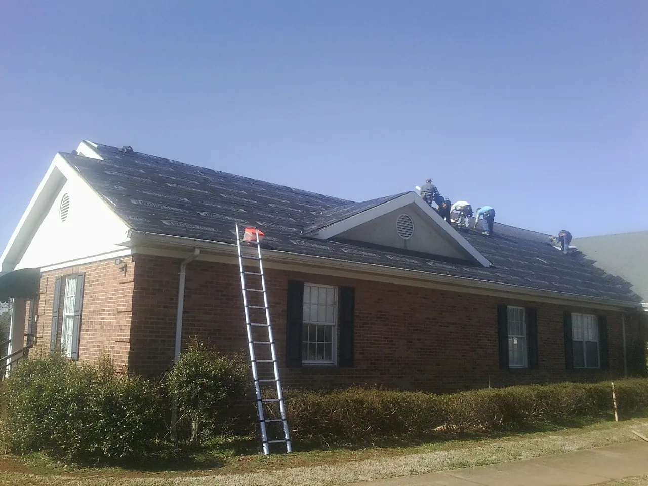 Crew tearing shingles off a brick ranch roof with a ladder set — Emergency Roof Repair work by our crew in Bakersfield