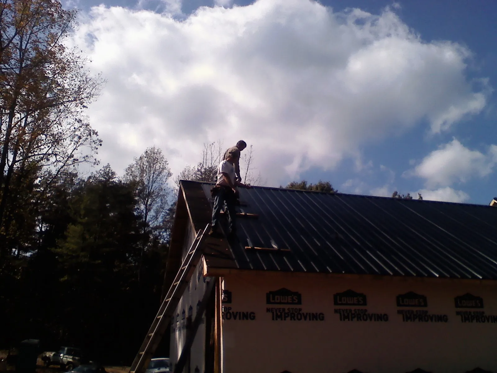 Roofer fastening dark metal panels high against a cloudy sky, from a Roof Inspection job in Bakersfield